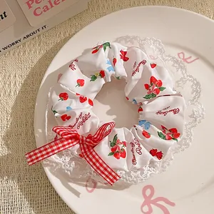 Detail of blue polka dot scrunchie with strawberry print, lace trim, and a red bow
