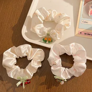 Detailed view of three floral scrunchies with fruit and flower charms on a tray