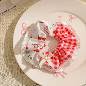 Detail of strawberry print hair scrunchie with red plaid fabric and lace trim bow