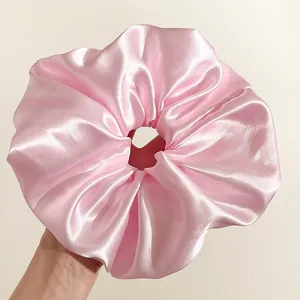 Dettaglio ravvicinato di un grande elastico scrunchie in raso rosa con trama liscia