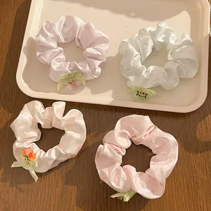 Close-up of four floral satin hair scrunchies with ribbon bows and flower charms