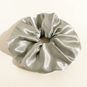 Dettaglio dell'elastico scrunchie gigante in raso argento con trama setosa e pieghe