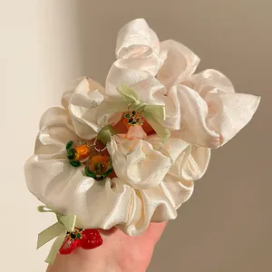 Detail of cream silk scrunchie with green bow and strawberry resin charms