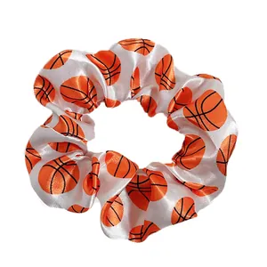 Close-up of a white satin scrunchie with a vibrant orange basketball print pattern
