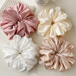 Close-up of four oversized satin scrunchies in cream and champagne on a white surface