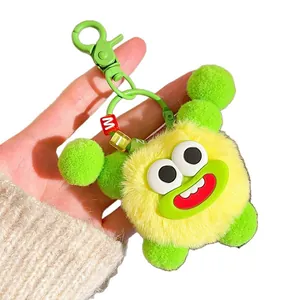 Funny yellow plush monster keychain with fuzzy texture and green mouth, hand-held view