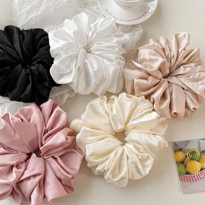 Detail showing five assorted oversized satin scrunchies in neutral and pastel shades