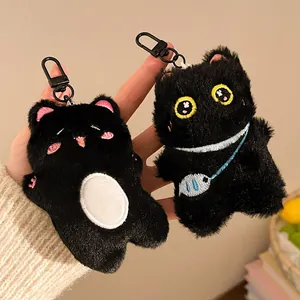 Close-up of two cute black plush cat keychains with blue fish bag and soft fur details