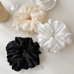 Close-up of oversized satin scrunchies in cream, white and black with silky texture