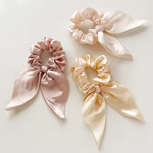 Detailed view of three satin bow scrunchies in pink, champagne and cream colors