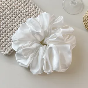 Detail of an oversized white satin scrunchie with a soft pearlescent sheen and pleated texture