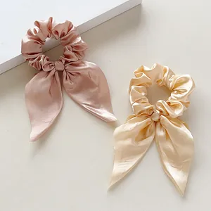 Detail of two silk satin bow hair scrunchies in soft pink and champagne gold