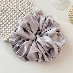 Close-up of oversized silver-grey satin scrunchie with elegant pleated fabric texture