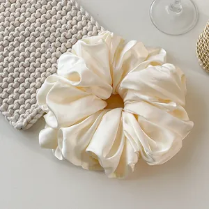 Macro detail of creamy satin scrunchie showing glossy fabric texture and soft pleats