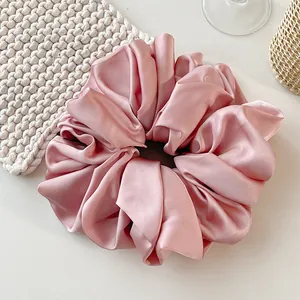 Detail view of pink satin scrunchie with soft silk texture and elegant pleats on white desk