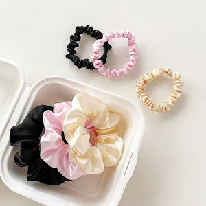 Detail of silk satin scrunchies in black, pink and champagne colors in a white box