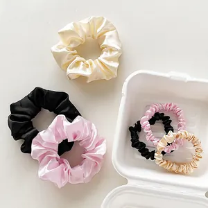 Detail of satin scrunchie set in ivory and champagne gold within a textured white box