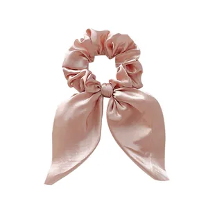 Detailed view of champagne pink satin bow scrunchie with long ribbons and silky texture