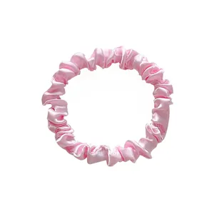Close-up of pink satin scrunchie showing glossy fabric texture and elastic pleats