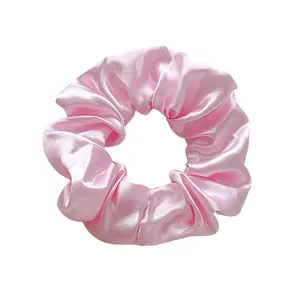 Close-up of a soft pink satin scrunchie with a silky texture and elegant fabric folds