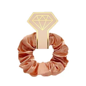 Detail van een roségouden satijnen scrunchie op een roze diamantvormige geschenkkaart