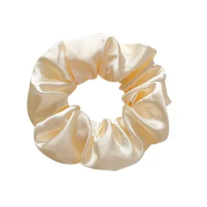 Close-up of champagne satin scrunchie showing glossy fabric texture and elegant pleats