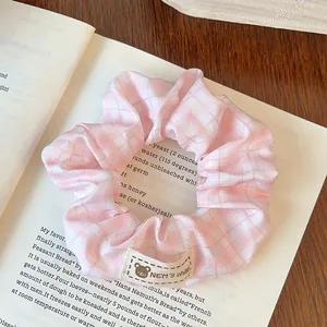 Detail shot of a pink and white checkered scrunchie with a bear tag on an open book