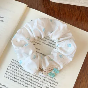 Detail of white scrunchie with blue tulips, fabric label, and mint bow on a book