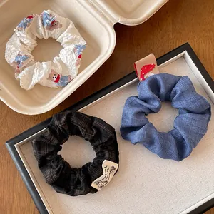 Detail of three aesthetic scrunchies with lace edges, bear prints, and plaid patterns