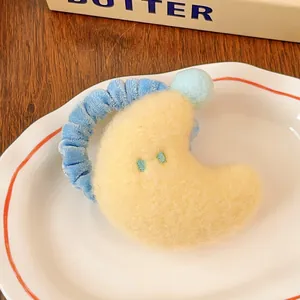 Gros plan d'un chouchou lune en peluche jaune avec anneau en velours bleu sur assiette blanche