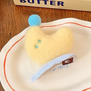 Détail d'une pince à cheveux lune en peluche jaune avec pompon bleu sur une assiette