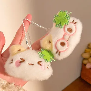 Close-up of soft white plush cat charms with clover accents and cute embroidered details