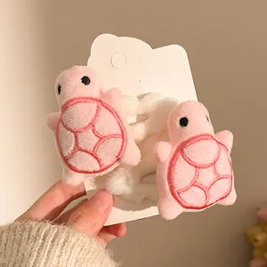 Detail of two pink plush turtle hair ties with red shell embroidery on a display card