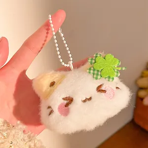 Close-up of a white plush cat keychain featuring an embroidered face and clover patch