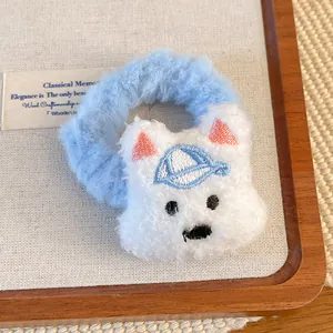 Close-up of plush West Highland dog hair scrunchie with blue hat detail on wooden tray