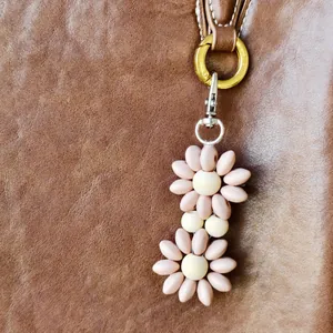 Pink daisy beaded bag charm with wooden center and silver clasp on leather bag