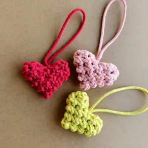 Détail de trois breloques cœurs au crochet en coton rouge, rose et jaune fait main