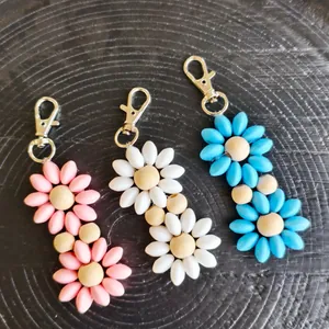 Close-up of colorful daisy flower keychains in pink, blue, and white on a wood background