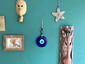 Turkish blue Evil Eye glass charm with wooden masks on a green wall background