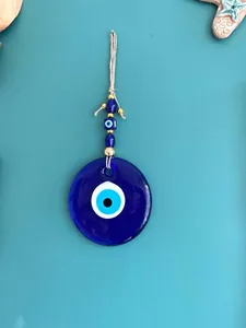 Macro detail of Turkish blue evil eye glass wall hanging with jute rope and gold beads