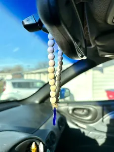 Macro view of gradient wooden beads and blue evil eye charm hanging on a car rear view mirror