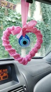 Detail showing handwoven pink heart with blue Evil Eye charm hanging on car mirror
