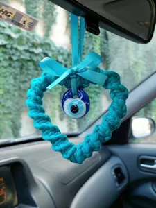 Detail of hand-woven blue heart-shaped evil eye car charm with a ribbon bow on mirror