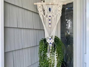 Detail of woven macrame plant hanger with blue evil eye beads on a rustic wall