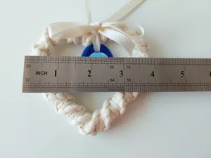 Macro shot of hand-woven cream heart pendant with evil eye bead and blue silk bow detail
