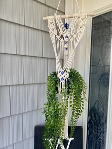 Detail of bohemian macrame plant hanger with evil eye beads and natural wood support