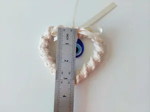 Macro shot of a handmade woven heart evil eye charm with ruler showing 3.5-inch width