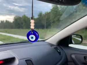 Detail of blue evil eye car hanging charm with woven rope and wooden beads on mirror
