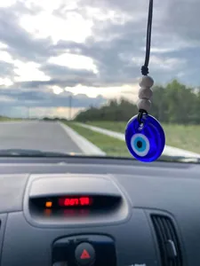 Detail of hand-woven car pendant with blue evil eye glass bead and white wooden accents