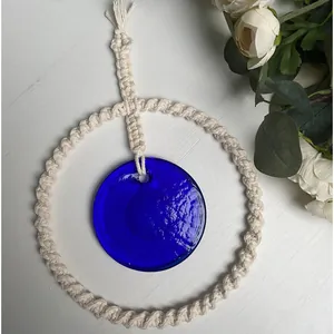 Dettaglio di decorazione murale in macramè con malocchio in vetro blu su legno bianco